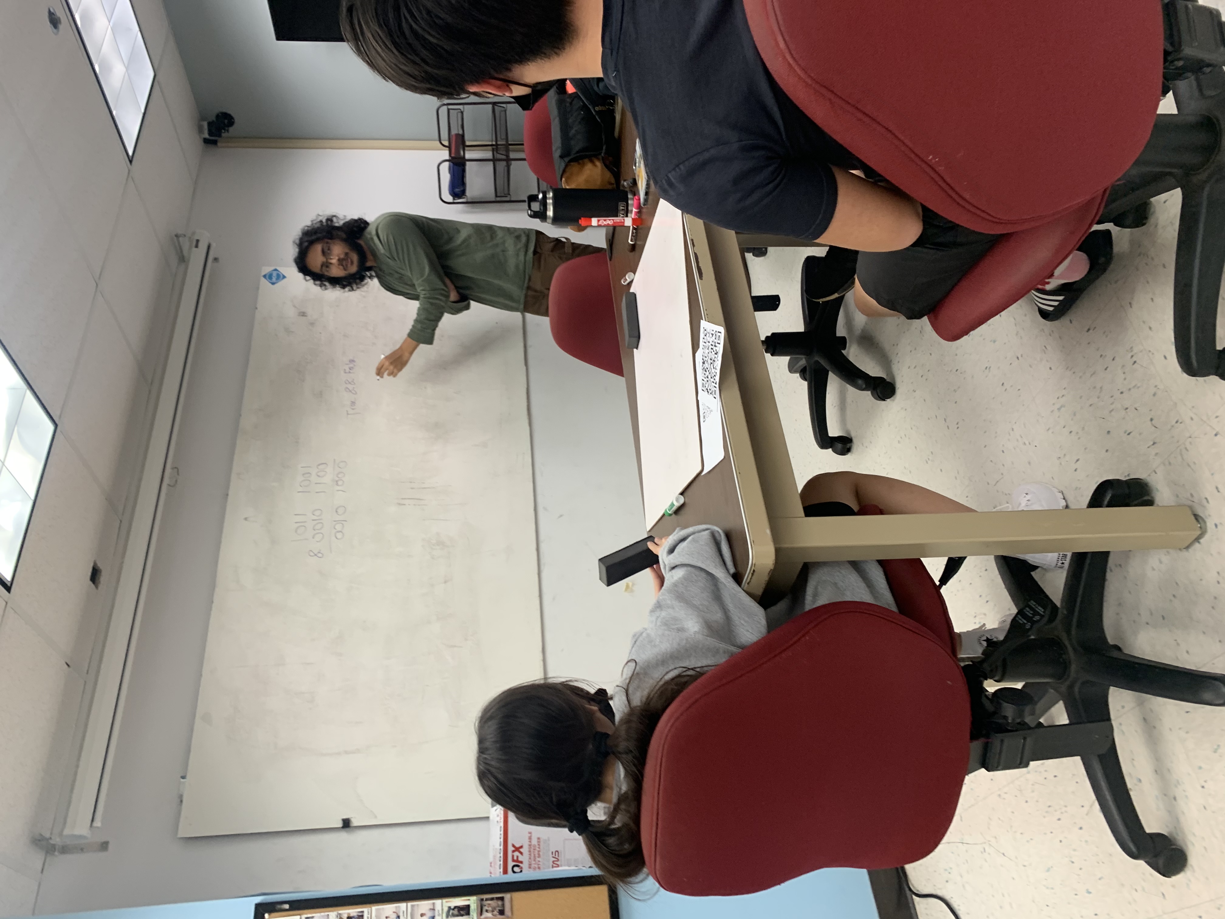 A man lecturing to two students in front of a whiteboard